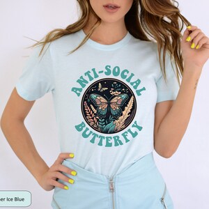 May include: A light blue t-shirt with a graphic of a butterfly in a circle with the text "Anti-Social Butterfly" in a teal color.