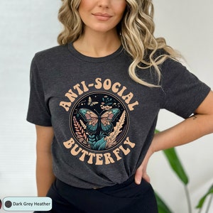 May include: A dark grey heather t-shirt with a graphic of a butterfly in a circle with the text "Anti-Social Butterfly" in a retro font.