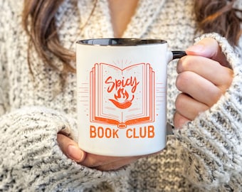 May include: White ceramic mug with a black rim and handle. The mug features an orange graphic of a book with flames and the text "Spicy Book Club".