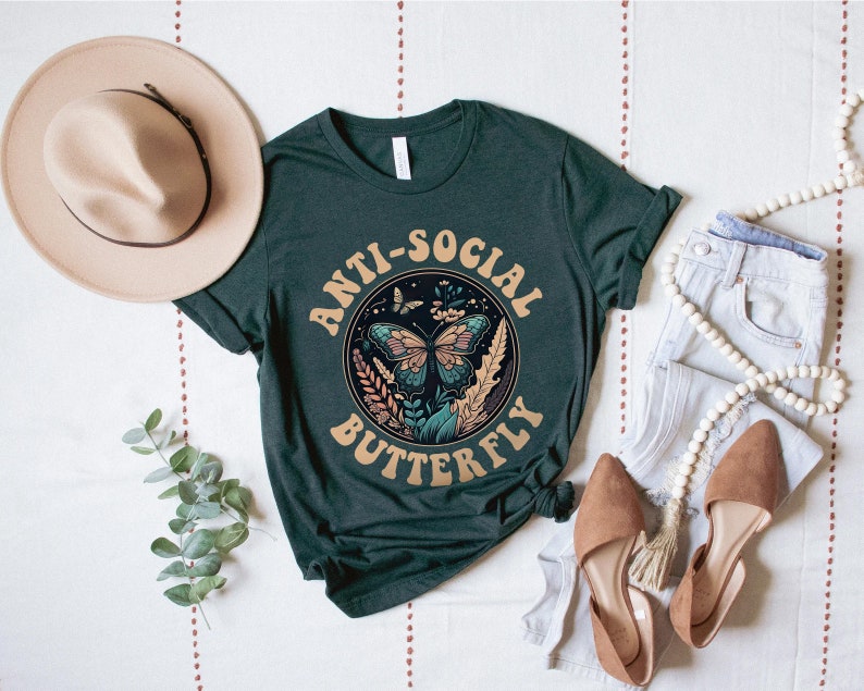 May include: A dark green t-shirt with the text "Anti-Social Butterfly" in a retro font. The text is surrounded by a circle with a butterfly and floral design.