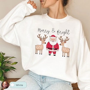 May include: White sweatshirt with a festive design featuring Santa Claus, two reindeer, and the text "Merry & Bright" in black. The Santa Claus illustration is in red and white, and the reindeer are brown.