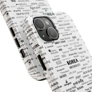 以下が含まれることがあります： 白の携帯電話ケース。黒と白の韓国をテーマにしたデザイン。ケースには、「KOREA」、「SEOUL」、「HAN RIVER」など、さまざまな韓国語の単語やフレーズが使用されています。このケースはスマートフォンにフィットするように設計されており、カメラとボタン用の切り欠きがあります。