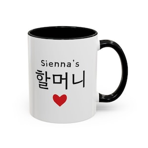 May include: White ceramic mug with a black interior and handle. The mug features the text "Sienna's" in black, followed by Korean characters and a red heart. The mug is designed for hot beverages.