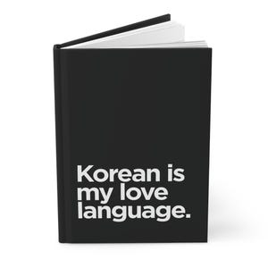 May include: Black journal with the text "Korean is my love language" in white. The journal is open, revealing white pages. The cover is solid black, and the text is centered.