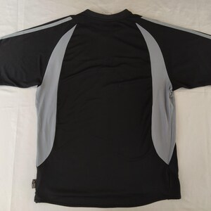 May include: Black athletic t-shirt with grey side panels and sleeve detailing. The short-sleeved top has a crew neck and is made of a lightweight, breathable fabric. The back of the shirt is visible, showing the design and construction.