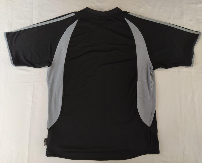 May include: Black athletic t-shirt with grey side panels and sleeve detailing. The short-sleeved top has a crew neck and is made of a lightweight, breathable fabric. The back of the shirt is visible, showing the design and construction.