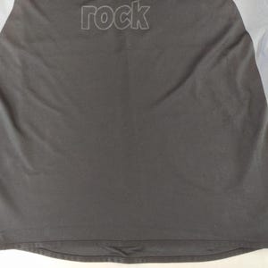 May include: Black athletic shirt with grey mesh side panels. The word "rock" is embroidered across the upper back in a darker shade of grey. The shirt has a crew neck and short sleeves.