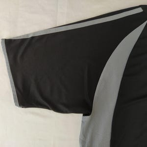 May include: Black athletic shirt with grey accents. The short sleeve has a grey trim. A grey mesh panel runs down the side of the shirt. The shirt is made of a lightweight, breathable material.