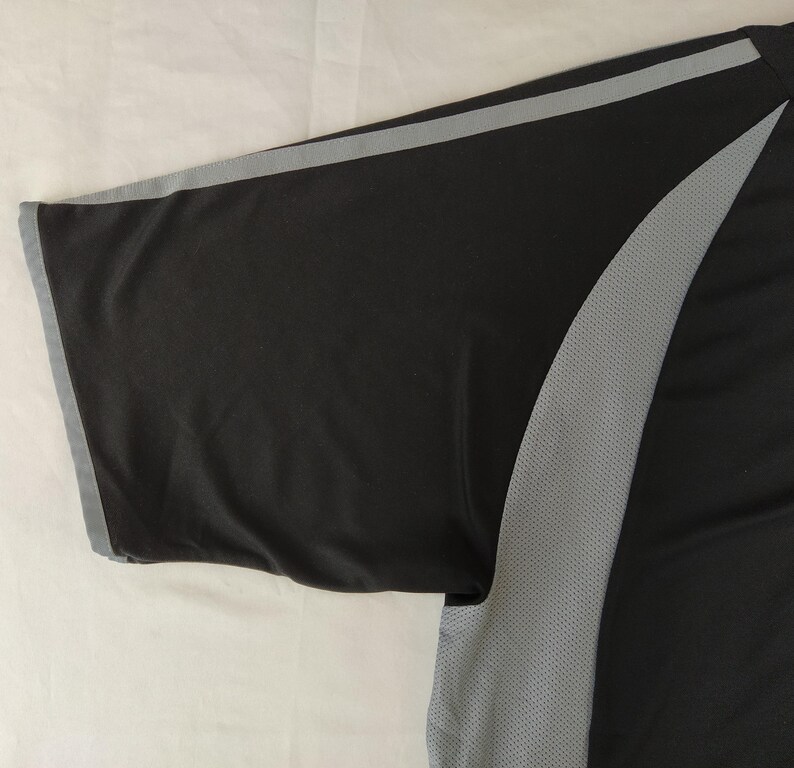 May include: Black athletic shirt with grey accents. The short sleeve has a grey trim. A grey mesh panel runs down the side of the shirt. The shirt is made of a lightweight, breathable material.