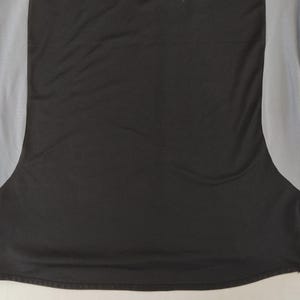May include: Black athletic top with grey mesh side panels. The shirt features a curved hem and a small tag on the lower left. The fabric looks like moisture-wicking material, suitable for sports and exercise activities.