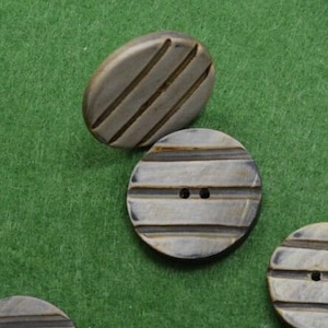 May include: Assortment of round, brown and black buttons with a striped pattern. The buttons have two holes each.