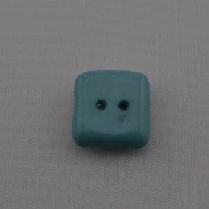 May include: A square teal button with two holes.
