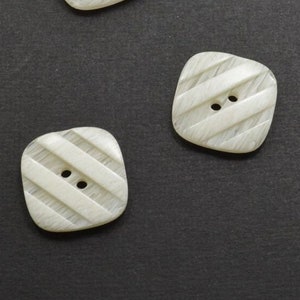 May include: Three white square buttons with a striped pattern and two holes each.