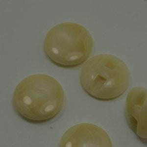 May include: Five white round buttons with a smooth, shiny finish. The buttons have a slight swirl pattern and a hole in the center.