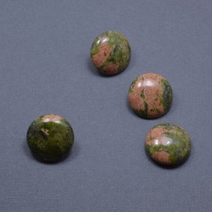 May include: Four round unakite stones with a polished finish. The stones display a mix of green and pink hues, with a speckled pattern. The stones are arranged on a gray surface.