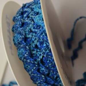 May include: A spool of blue and turquoise fuzzy trim. The trim is wound around a white spool with the word "Liberty" printed on it.