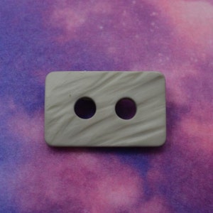 May include: A gray plastic button with two holes. The button has a textured surface.
