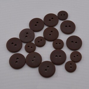 May include: A collection of brown plastic buttons of various sizes. The buttons have two holes each.