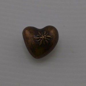 May include: A heart-shaped, brown metal ornament with a gold edelweiss flower design.
