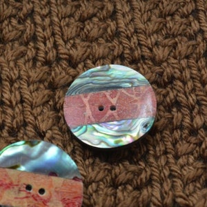 May include: Two iridescent abalone shell buttons with a red and brown patterned band. The buttons have two holes.