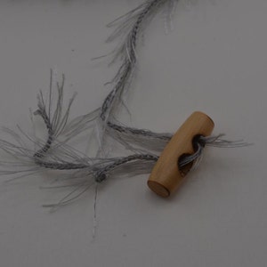 May include: A wooden toggle button with a hole in the center, attached to a gray and white fuzzy cord.