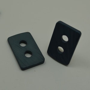 May include: Two dark gray rectangular buttons with two holes each. The buttons have a textured surface.