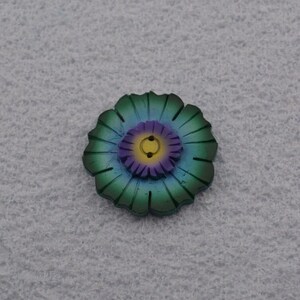 May include: A green, blue, and purple flower-shaped button with a yellow center.