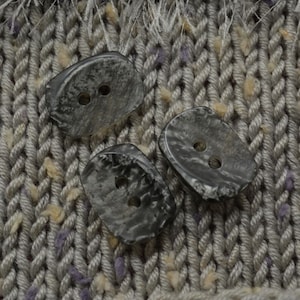 May include: Three gray, mottled, plastic buttons with two holes each. The buttons are on a gray knitted fabric.