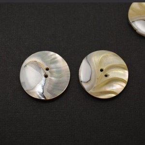 May include: Two round, white and beige mother of pearl buttons with two holes each.