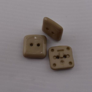 May include: Three beige plastic square buttons with two holes each. The buttons are smooth and have a slightly glossy finish.