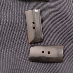 May include: Two black horn buttons with two holes each. The buttons are rectangular with rounded edges.