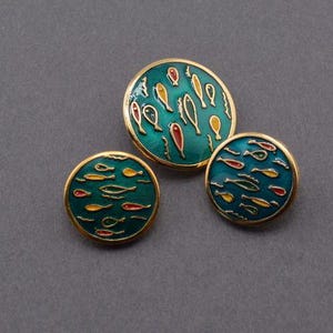 May include: Three gold-toned buttons with a teal blue background and a design of yellow and red fish.
