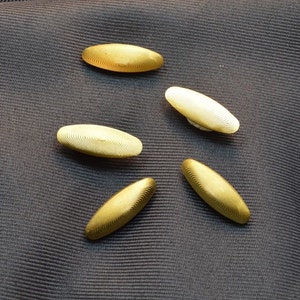 May include: Five gold-colored oval-shaped buttons with a textured surface.
