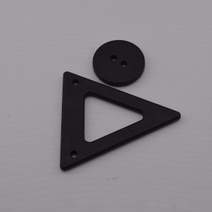 May include: Two black buttons, one round and one triangular. The round button has two holes. The triangular button has three holes.