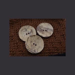 May include: Three brown coconut shell buttons with two holes each. The buttons are on a brown knitted fabric.