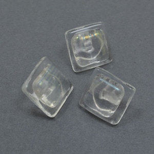 May include: Three clear square buttons with iridescent details. The buttons are made of glass and have a smooth, polished finish.