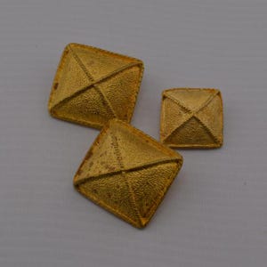 May include: Three gold-toned metal pyramid-shaped buttons with a textured surface.