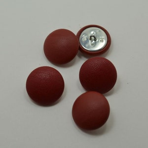 May include: Five red leather buttons with a silver shank. The buttons have a textured surface.