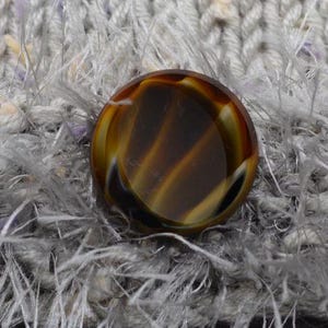 May include: A brown and black button with a striped pattern. The button is made of plastic and has a shiny finish.