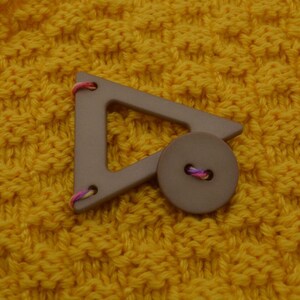 May include: A brown triangle-shaped button with a smaller round button in the center. The buttons are attached to a yellow knitted fabric.
