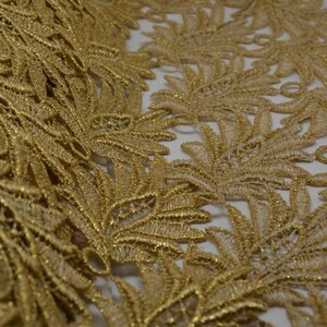 May include: Gold lace trim with a delicate floral pattern. The lace is made of a fine mesh fabric with a metallic sheen.