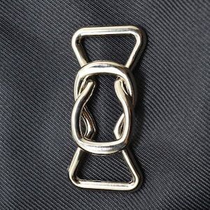 May include: A silver metal slider buckle with a looped design. The buckle is commonly used for straps and belts.