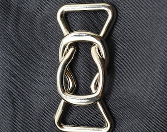 Può includere: Una fibbia scorrevole in metallo argentato con un design ad anello. La fibbia è comunemente usata per cinturini e cinture.