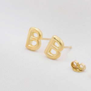 Może przedstawiać: Para złotych kolczyków z literą 'B' i dopasowanymi zapięciami.