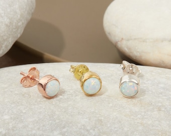 May include: Three opal stud earrings in different metal finishes: rose gold, gold, and silver. The earrings are displayed on a white stone surface.