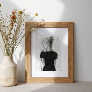May include: A framed black and white drawing of a person in a black dress, with a light gray background. The frame is made of natural wood.