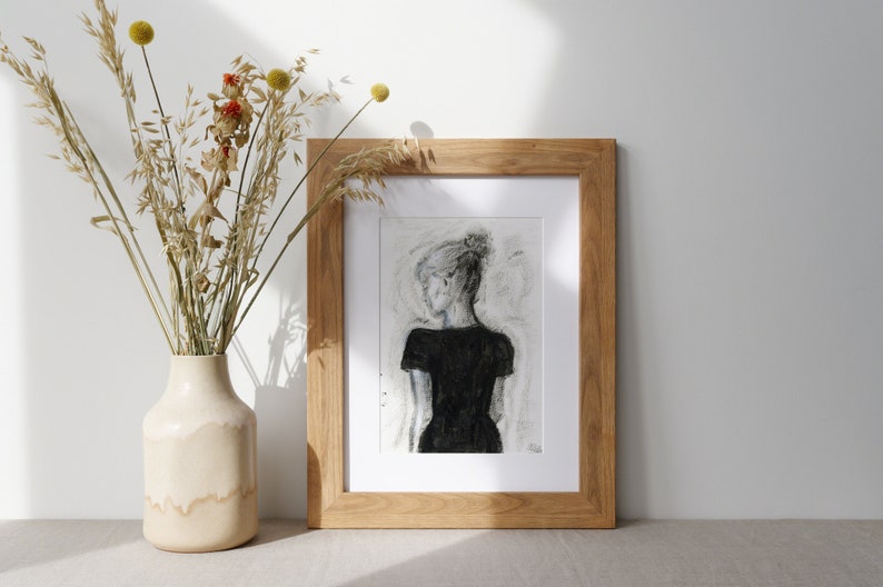 May include: A framed black and white drawing of a person in a black dress, with a light gray background. The frame is made of natural wood.