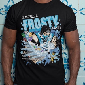 May include: A black t-shirt with a graphic print of a blue character holding a snowball. The text "Sub-Zero's Frosty Flakes" is printed on the shirt. The graphic also includes the text "Now with mini marshmallows" and "Prize inside".