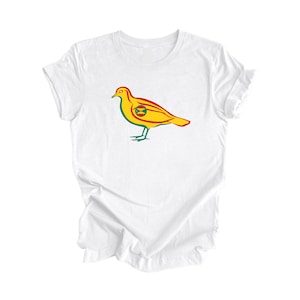 Może przedstawiać: Biała koszulka z nadrukiem stylizowanego żółtego ptaka. Ptak ma na piersi zielono-czerwone koło z żółtym X w środku.