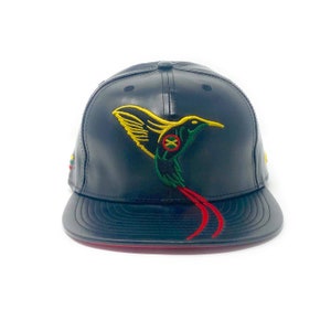 May include: Black leather baseball cap with a red brim and an embroidered hummingbird with yellow, green, and red accents. The hummingbird has a small circle with a red X and a yellow circle inside.
